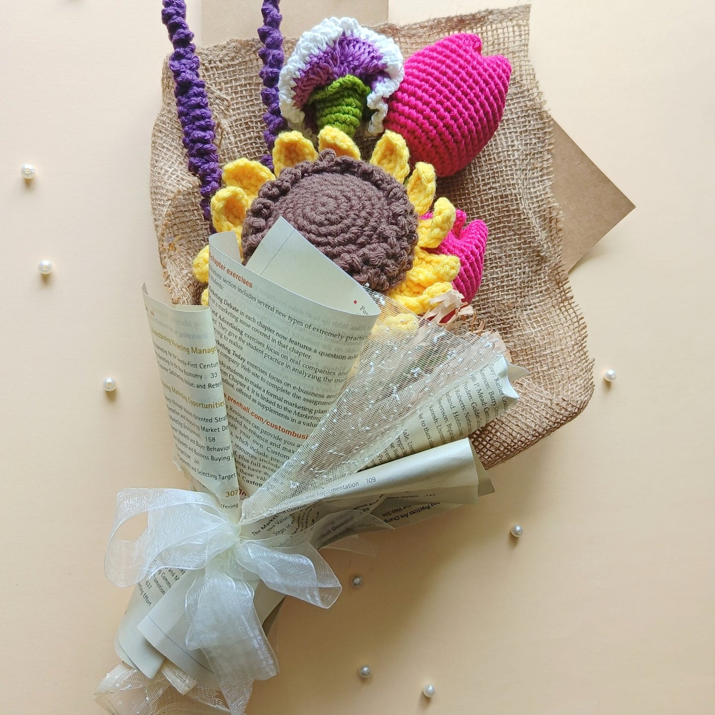 Bouquet of crocheted flowers wrapped in newspaper with a white ribbon on a beige background
