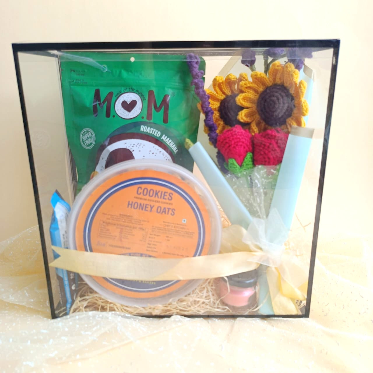 Gift basket with cookies,crochet  sunflower and rose bouquet, and other items in a clear box.