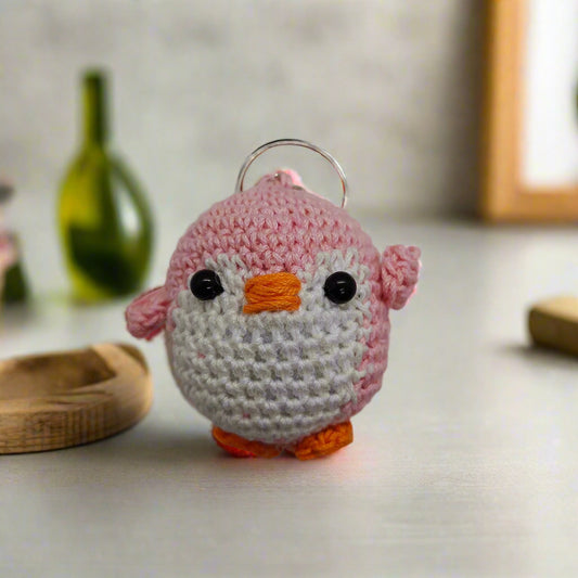 Crocheted penguin keychain with pink body, black eyes, and orange beak and feet