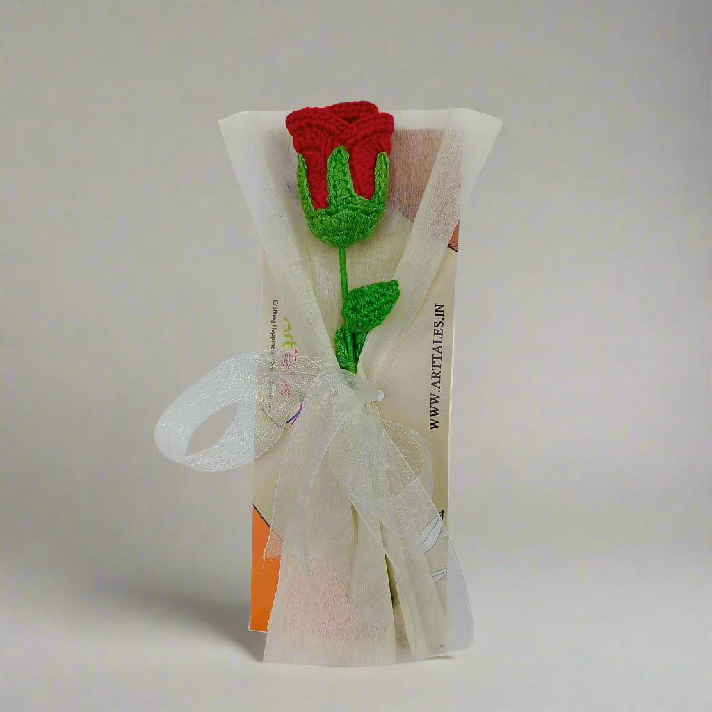 Crocheted red rose with green leaves on a clear plastic bag against a white background