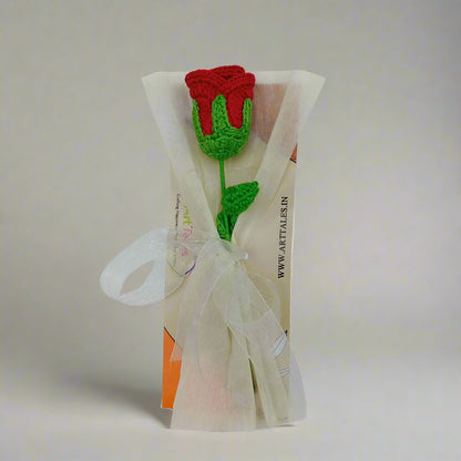 Crocheted red rose with green leaves on a clear plastic bag against a white background