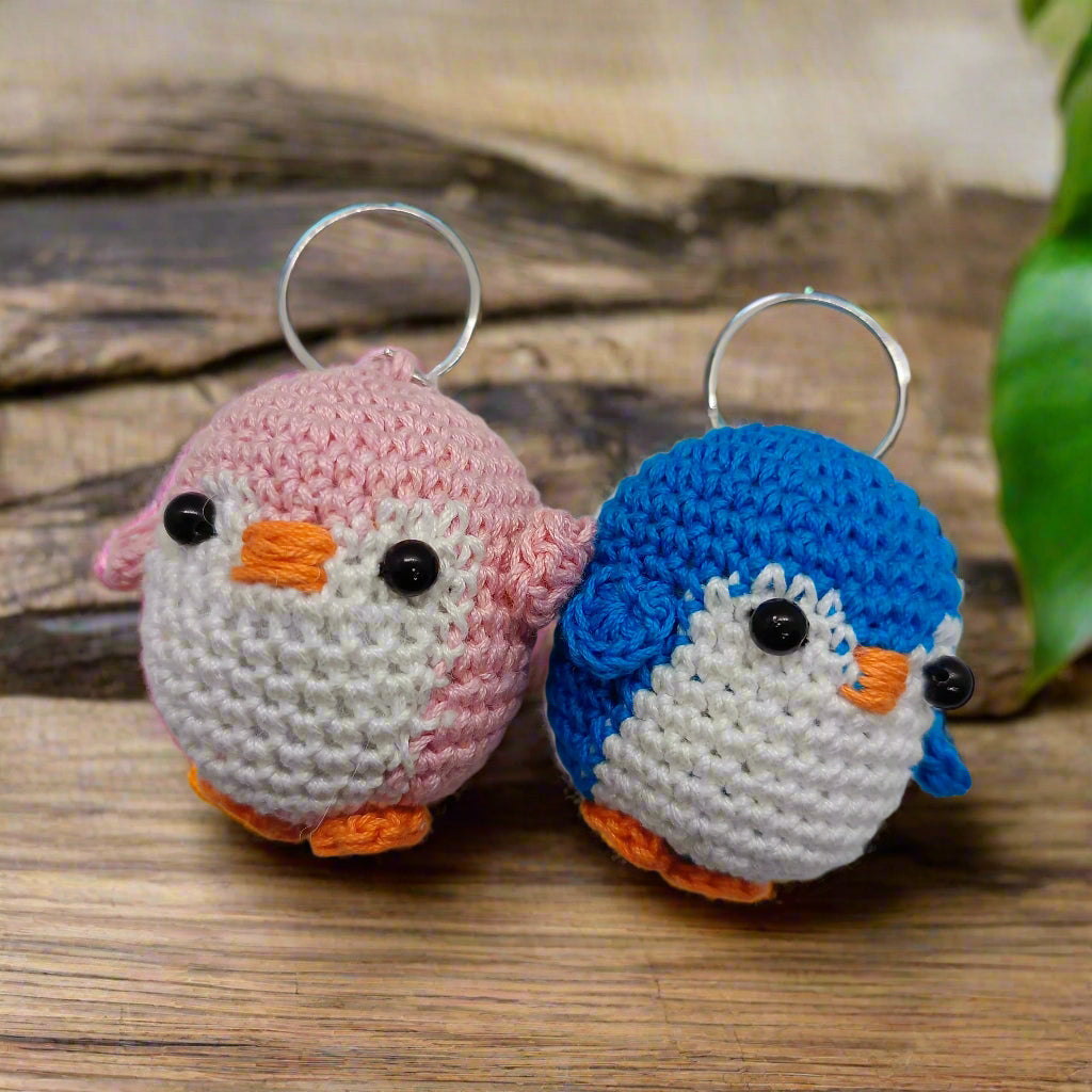 Two crocheted bird keychains, one pink and one blue, on a white background.